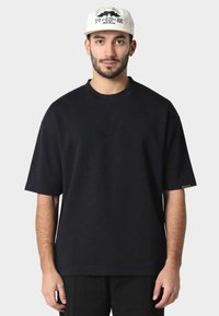 Černé oversized tričko s krátkými rukávy, kulatým výstřihem a jemným detailem boční etikety, vyrobené z texturované bavlněné tkaniny.
