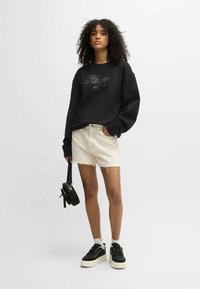 Felpa nera con scritte argentate, abbinata a pantaloni shorts in denim beige chiaro con bordi sfrangiati. Sneakers nere con plateau e una borsa nera piccola.