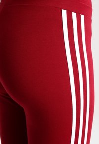 Röda träningsleggings med en slät yta, hög midja och tre vita vertikala ränder längs sidan.