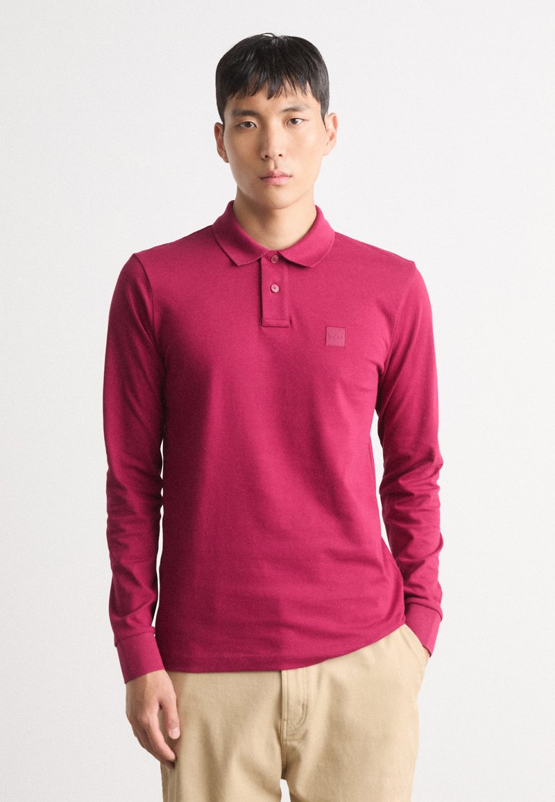 Lange mouwen, poloshirt in diep magenta, gemaakt van zacht materiaal, met een kraag en een klein merklabel op de linkerborst.