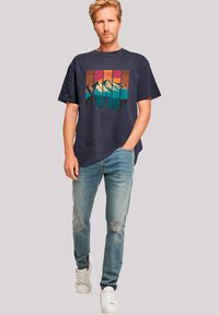 Marine T-shirt met kleurrijke bergafbeelding; gecombineerd met lichtblauwe versleten jeans en witte sneakers. Eenvoudig, casual pasvorm ontwerp.