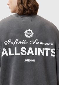 Szary, oversize'owy sweatshirt z napisem "Nieskończone Lato" oraz "ALLSAINTS LONDYN" w postarzonym białym tekście na plecach, z okrągłą grafiką powyżej.