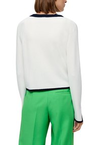 Witte cropped trui met een marineblauwe kraag, gecombineerd met groene broeken. Zacht materiaal, lange mouwen en contrasterende accenten.