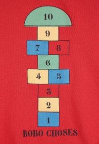 Grille de marelle avec des cases numérotées de 1 à 10 en bleu, rouge, vert et beige sur un fond rouge avec le texte « BOBO CHOSES » en dessous.
