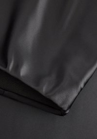 Schwarze, strukturierte Tasche mit glänzender Oberfläche und einem Stoffreißverschluss-Akzent. Sie hat eine glatte Oberfläche mit subtilen Falten und Nähten.
