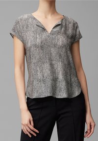 Blouse à manches courtes avec un motif noir et blanc, présentant un décolleté en V, une texture douce et un design aérien, portée avec un pantalon noir.