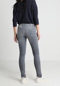 Harmaat kapeat farkut korkealla vyötäröllä, valmistettu denimmistä. Ominaisuudet takataskut ja ne on yhdistetty löysään tummansiniseen paitaan sekä valkoisiin tennareihin.