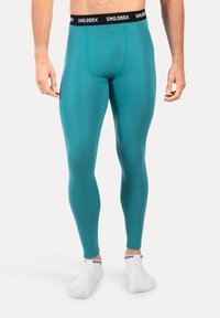 Mężczyzna w turkusowych legginsach z czarnym pasem Smilodox i białymi skarpetkami za kostkę na białym tle.