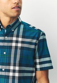 Kurzärmliges Hemd mit Knopfleiste, das ein blau-grünes Karomuster mit grauen und weißen Akzenten aufweist, gefertigt aus leichtem Stoff.