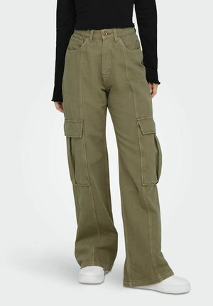 Pantalon cargo ample couleur olive avec poches à rabat, porté avec un haut à manches longues noir et des baskets blanches.