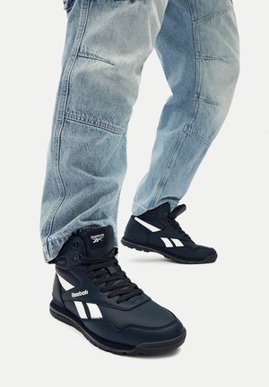 Zapatillas negras de caña alta con detalles en blanco, con parte superior de cuero liso, cierre de cordones y suela de goma texturizada, usadas con vaqueros azul claro.