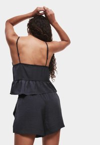 Černý top bez rukávů s peplum lemem a nastavitelnými ramínky, kombinovaný s šortkami; hladká textura a uvolněný střih.