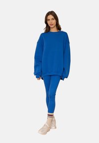 Niebieska, oversize'owa bluza zestawiona z dopasowanymi niebieskimi legginsami. Tkanina wydaje się miękka i teksturowana, z luźnym krojem i minimalnym wykończeniem.