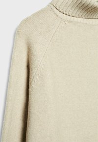 Maglione beige a collo alto lavorato a maglia con dettagli a punto testurizzato sulle spalle e sulle maniche, mostrato in primo piano su uno sfondo semplice.