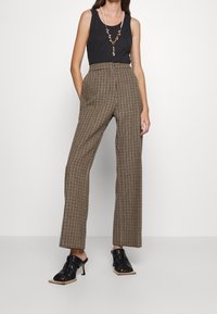 Höga bruna och beige rutiga byxor med en bred benprofil, kombinerat med en svart linne och svarta klackskor.