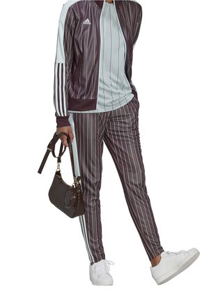 Bordo i jasnoniebieski dres w paski wykonany z gładkiego materiału, zestawiony z małą brązową torebką w wzór gadziej oraz białymi sneakersami.