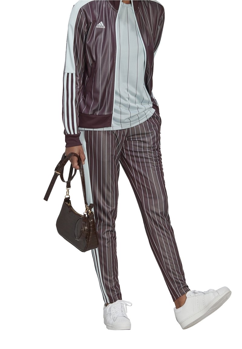 Bordeaux- und hellblaue gestreifte Trainingsanzug aus glattem Stoff, kombiniert mit einer kleinen braunen Handtasche im Reptilienmuster und weißen Turnschuhen.