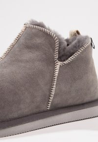 Sive čizme do gležnja od suede materijala s mekim, pahuljastim oblogom. Sadrže kontrastne bijele šavove i mali tekstilni deo oko gležnja za lakše obuvanje.