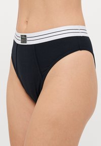 Svart bomulls-boksershorts med hvit stripete elastisk midjebånd. Har et merke foran og en jevn, myk tekstur.