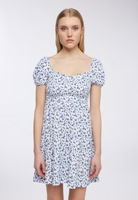 Abito bianco con motivo floreale blu, scollo quadrato, maniche a sbuffo e vita arricciata, che cade sopra il ginocchio.