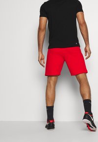 Röda shorts i bomullsblandning, knälånga med fåll. Bärs med en svart kortärmad skjorta och svarta strumpor med röda detaljer.