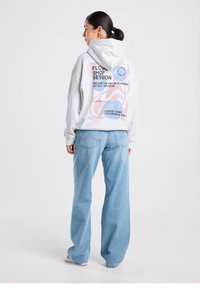 Sudadera con capucha gris con un diseño gráfico en la espalda en tonos rosa y azul, combinada con unos vaqueros anchos de algodón en azul claro. Material suave y casual.