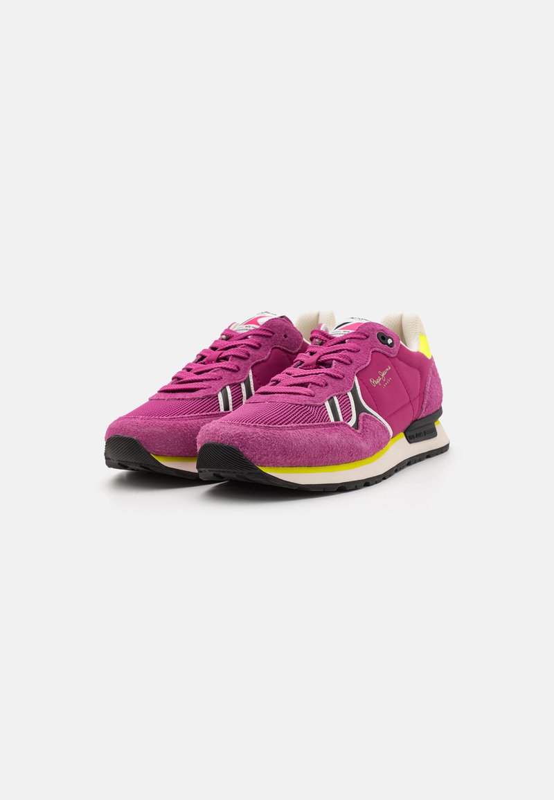 Rosa Wildleder- und Stoff-Sneaker mit schwarzer Gummisohle, gelben Akzenten und weißen sowie schwarzen Streifen an den Seiten. Schnürdesign.