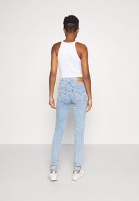 Vaaleansiniset korkeavyötäröiset farkut kapealla istuvuudella, joissa on nahkainen logopläsi takana, tavalliset taskut ja kulutettu viimeistely.