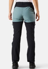 Kaksiväriset ulkoiluhousut, joissa on vaaleansininen yläosa ja mustat alaosat, sileä pinta, vetoketjulliset sivutaskut ja säädettävä vyötärö.