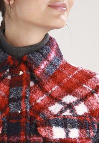 Rød og marineblå plaide faux fur jakke med en tekstureret overflade, stort krave og grå ribbet hals. Har knapper foran.