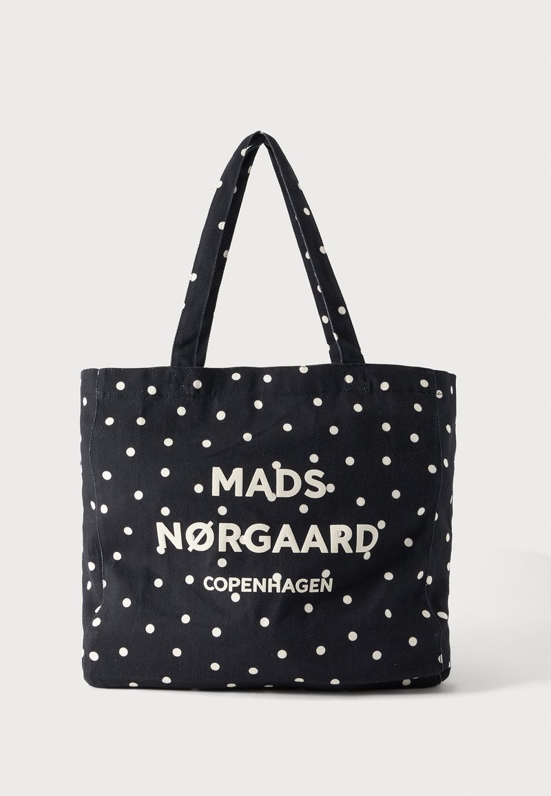 Μαύρη τσάντα tote με λευκές πουά, με το κείμενο "MADS NØRGAARD COPENHAGEN" σε λευκό στο μπροστινό μέρος και δύο λουράκια ώμου.