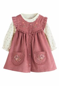 Frambozenkleurige corduroy jurk met ruche-schouders, bloemenborduursel op de lijf, en twee zakken met kantafwerking. Crème kleurige bloemetjes top met lange mouwen eronder.