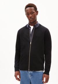 Zwarte zip-up trui met een ronde kraag, geribbelde manchetten en zoom. Draagt over een gestreept shirt met een gladde textuur en een aansluitend ontwerp.