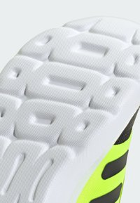 Schuhsohle mit einem strukturierten weißen Gummimuster, ausgestattet mit einem lebhaften gelben Obermaterial mit schwarzen Akzenten und Streifen.