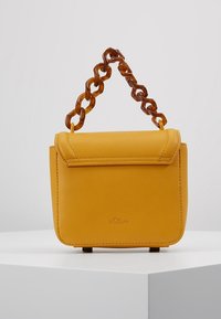 Sac à main en cuir synthétique jaune avec un rabat courbé, une texture lisse et une anse en chaîne en résine transparente chunky. Orné de "s.Oliver."