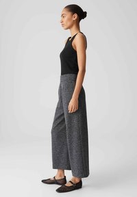 Schwarzes ärmelloses Oberteil, kombiniert mit grauen strukturierten weiten Hosen und schwarzen Mesh-Schuhen mit einem Riemen über dem Fuß. Schlichtes und modernes Design.