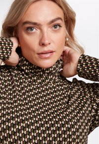 Maglione a maniche lunghe con collo alto, caratterizzato da uno sfondo scuro e un motivo geometrico in tonalità di verde, beige e viola. Tessuto morbido.
