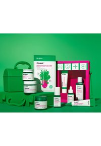 Dr. Jart+ Cicapair hudpleieprodukter arrangert på en grønn bakgrunn. Produktene inkluderer kremer, serum og et knallrosa etui.