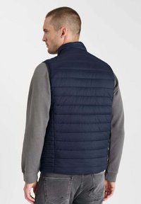 Marinblå pufferväst med horisontell quiltad design, hög krage och en slät textur, bärs över en grå långärmad skjorta.