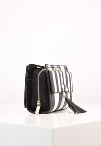 Borsa a strisce bianco e nero con finitura testurizzata, dotata di chiusura a patta, accessori in oro e dettaglio con nappina. Tasca laterale con zip.