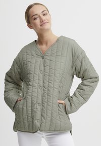 Nertinė, šviesiai alyvuogių spalvos striukė su V formos iškirpte, sagų užsegimu ir šoninėmis kišenėmis. Pasižymi tekstūruotu audiniu su vertikaliomis siūlėmis.