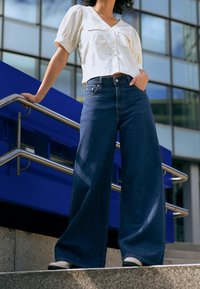 Szerokie dżinsy z ciemnoniebieskiego denimu w połączeniu z białą, krótkorękawową, zapinaną na guziki koszulą. Gładka tkanina i dopasowany krój, o eleganckim designie.