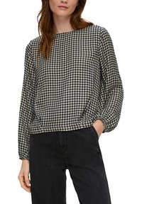 Schwarze und weiße Bluse mit Hahnentrittmuster, rundem Ausschnitt und langen, leicht puffigen Ärmeln, kombiniert mit dunklen Jeans.