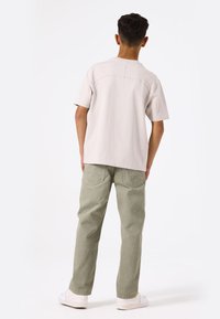 Camiseta de manga corta gris claro con cuello redondeado, combinada con pantalones holgados color oliva y zapatillas blancas.