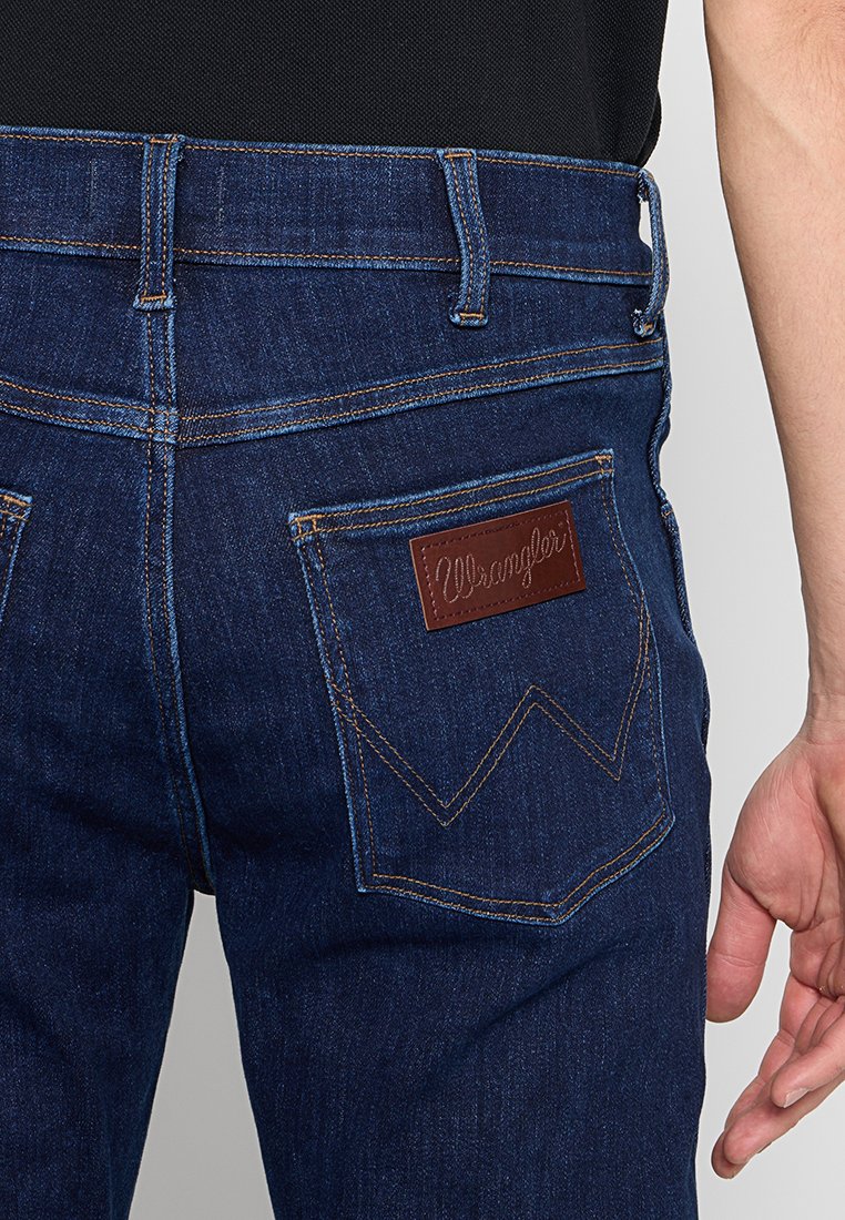 Dunkelblaue Denim-Jeans mit einem braunen Leder-Logopatch, sichtbaren Steppnähten und schrägen Gesäßtaschen. Verfügt über ein klassisches Fünf-Taschen-Design.
