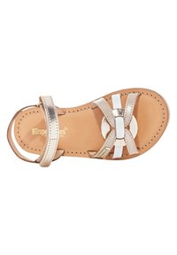 Sandal in cuoio chiaro con accenti bianchi e metallici, caratterizzata da un design a cinghie incrociate, dettaglio circolare e suola piatta.