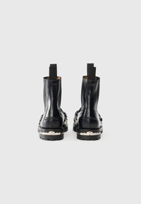 Bottes noires en cuir à chevilles avec panneaux élastiques sur les côtés, semelles texturées et accents en métal argenté. Design épuré et élégant avec une finition brillante.