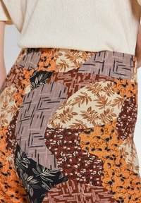 Patroonshorts van stof met verschillende aardetinten, waaronder oranje, bruin en crème, met ingewikkelde bloem- en geometrische ontwerpen.