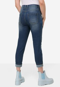 Tummansiniset farkut, joiden lahkeet on käännetty; niissä on kaksi takataskua ja sileä rakenne. Yhdistetty vaaleansinihin nilkkabootseihin.