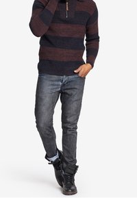 Maglione a maglia con righe blu scuro e bordeaux, colletto a zip a un quarto, abbinato a jeans in denim azzurro chiaro e stivali neri.